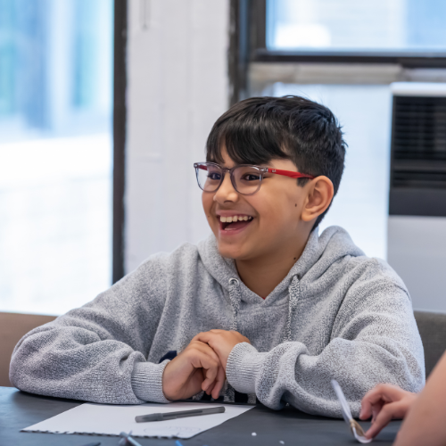 A boy with glasses smiles while sitting at a table